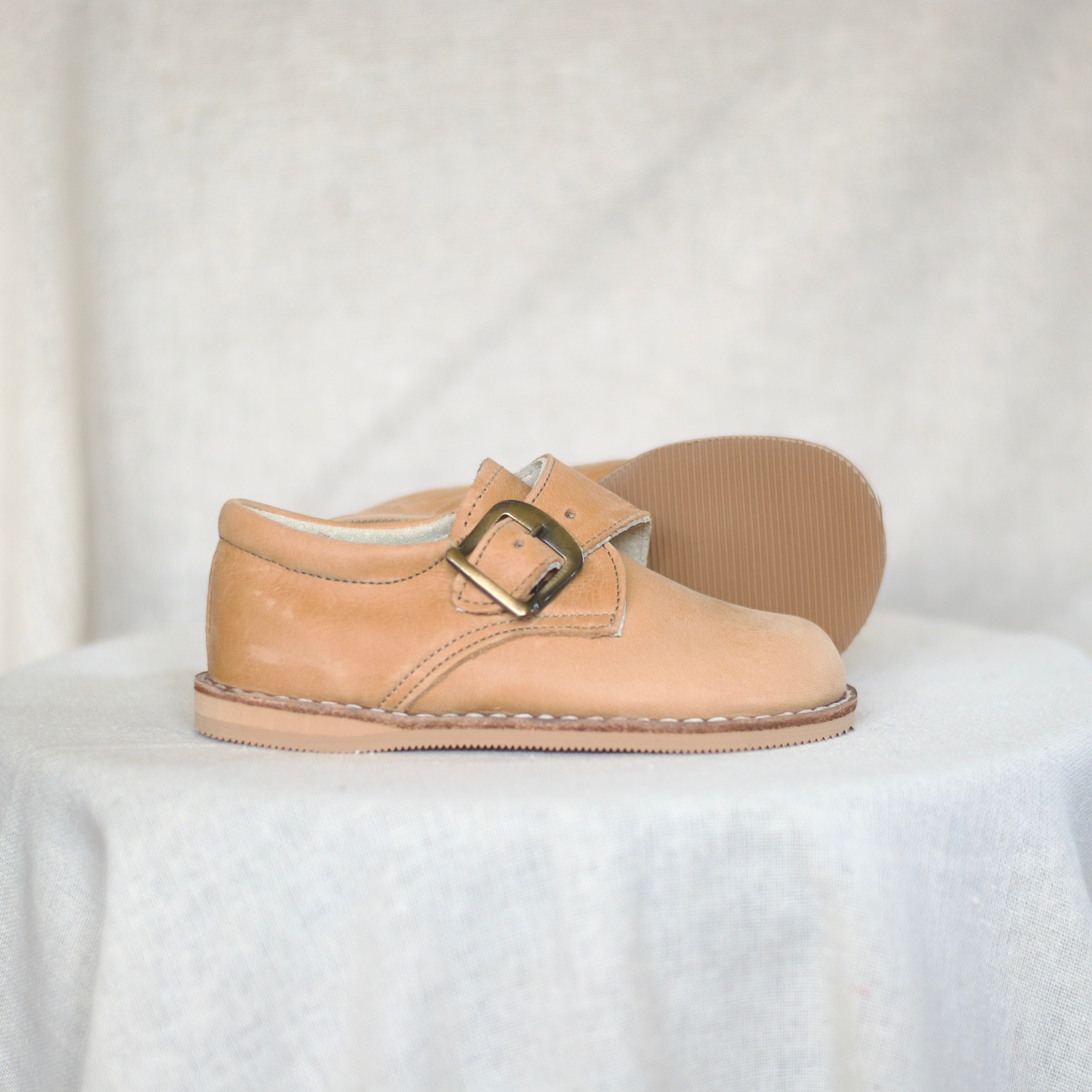 tan shoe with a buckle on a white background