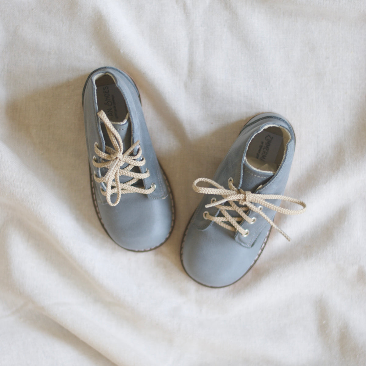 Pair of light blue shoes with beige laces on a white fabric background