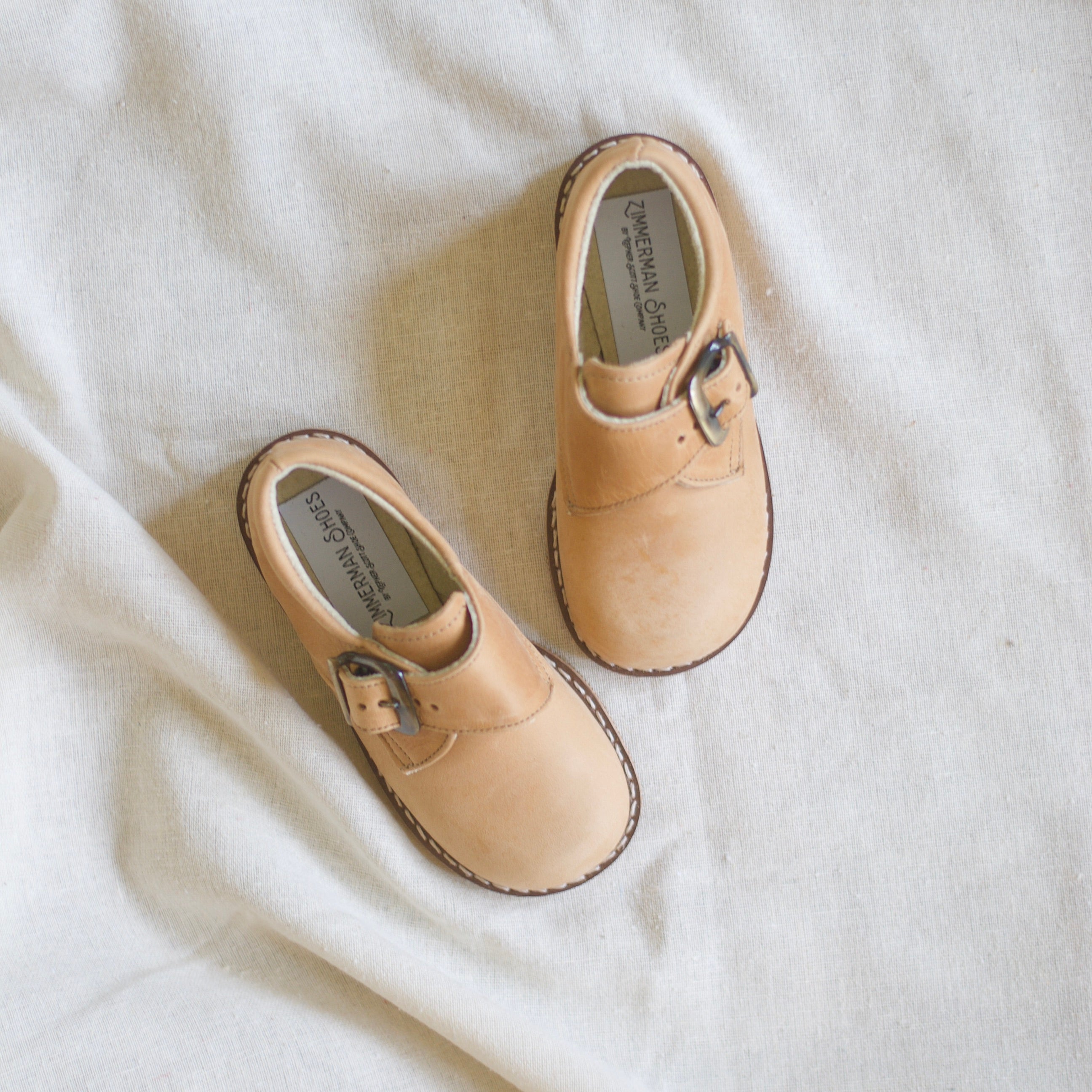 Pair of tan children's shoes on a white fabric background