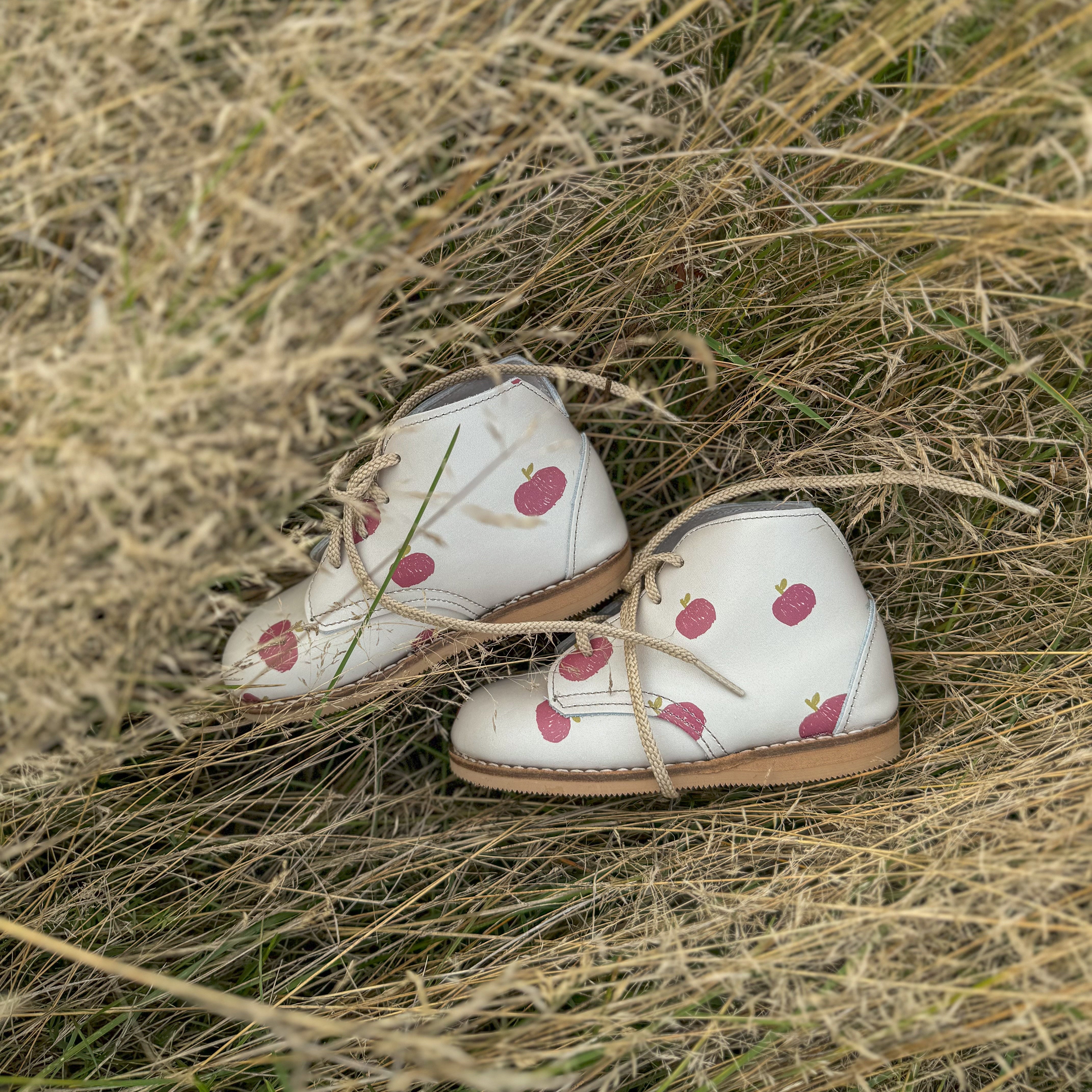 Pair of white shoes with an apple pattern on a grassy background