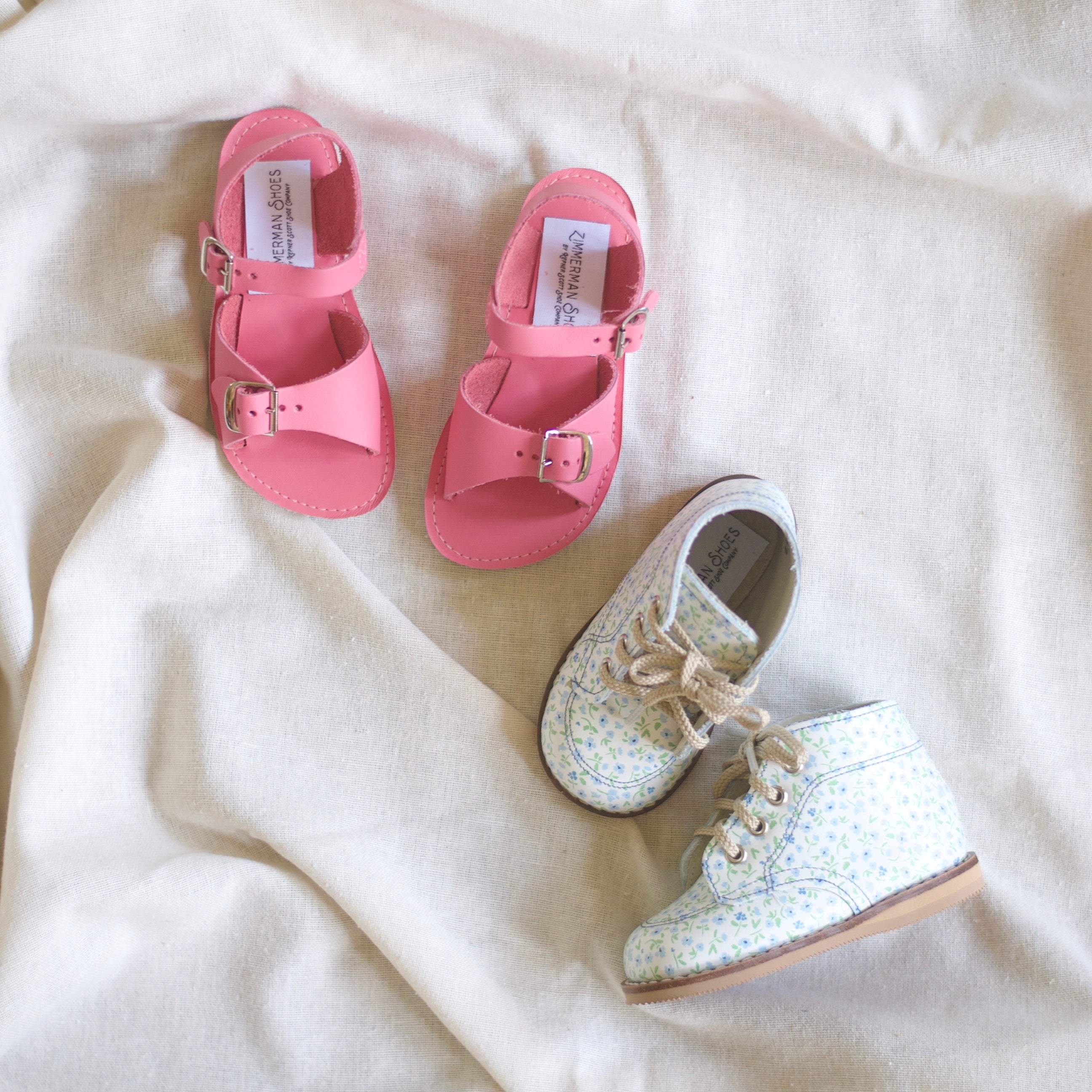 Pair of pink sandals and a white shoe with blue flowers on a light fabric background