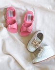 Pair of pink sandals and a white shoe with blue flowers on a light fabric background
