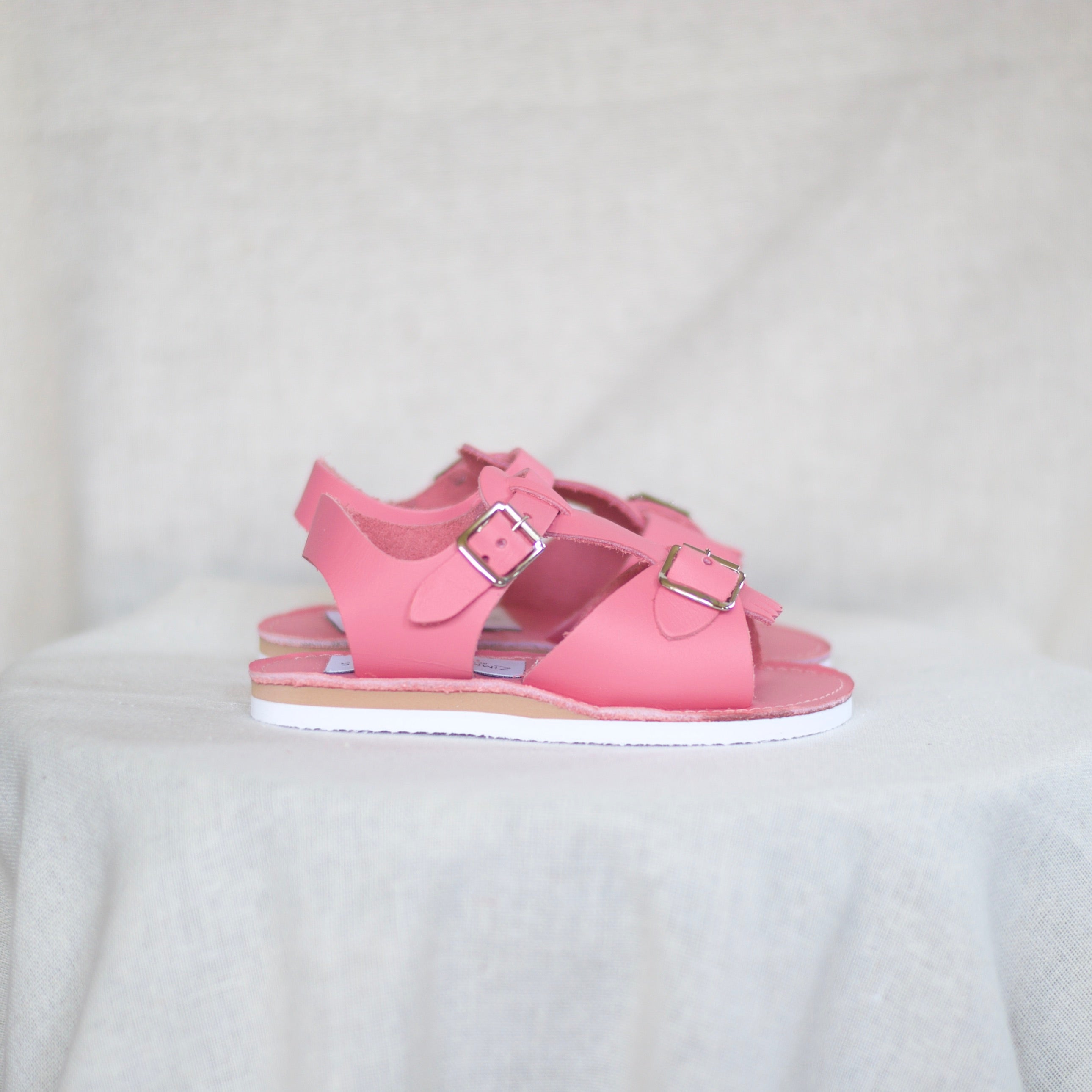Pink sandals with buckles on a white fabric background